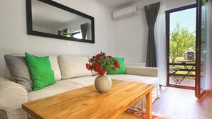 A living room with a wooden coffee table, a beige sofa with green cushions, a vase of red flowers, a large mirror, and a sliding glass door leading to an outdoor area. - Lagom Apartments (Rakovica)