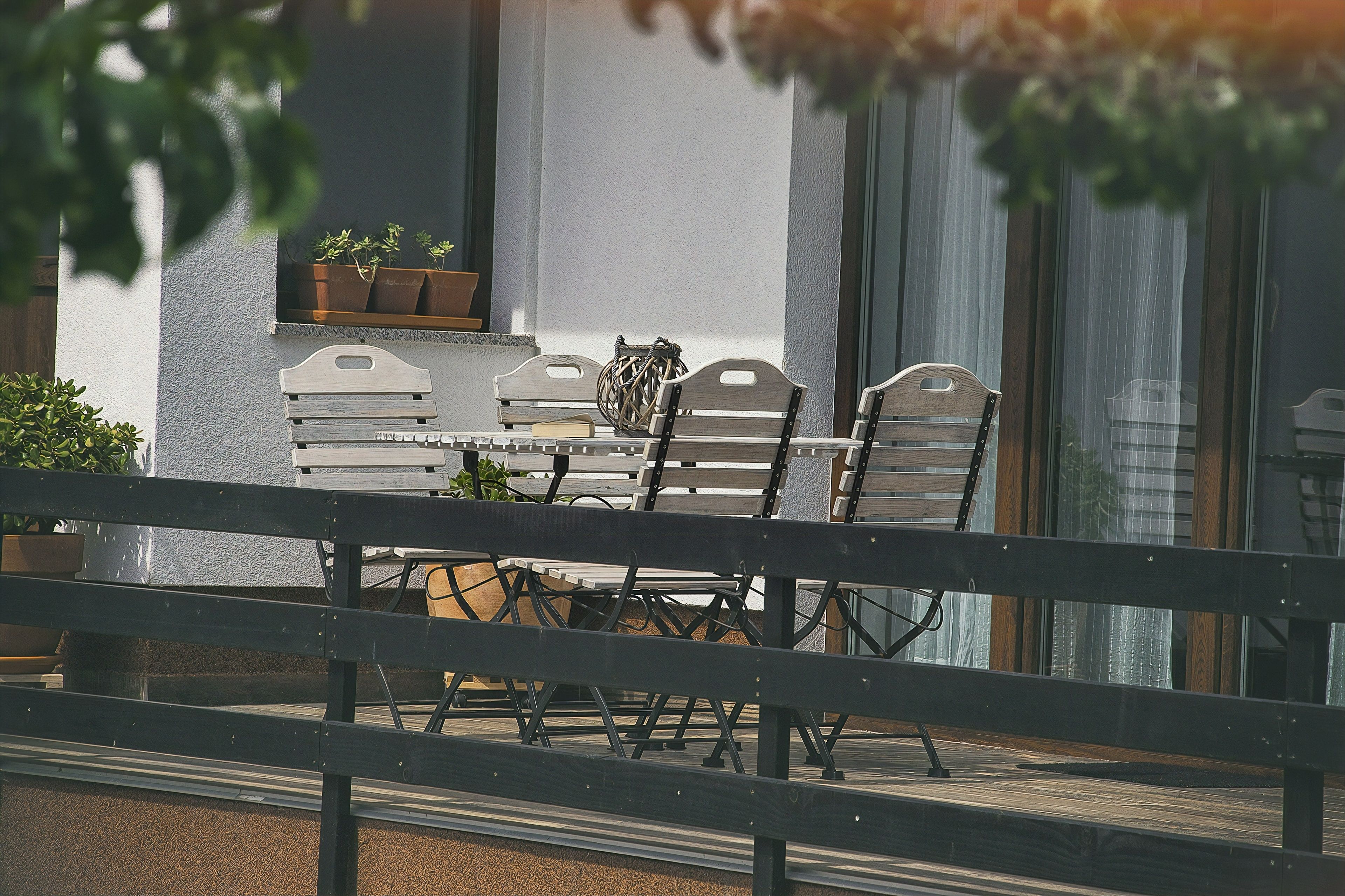 Eine Terrasse mit Tisch und Stühlen, Blumentöpfen und einem Fenster mit Jalousien.