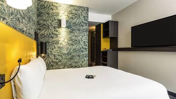 Habitació d'hotel amb un llit, un televisor penjat a la paret, una làmpada adossada i un paper pintat amb dibuixos.