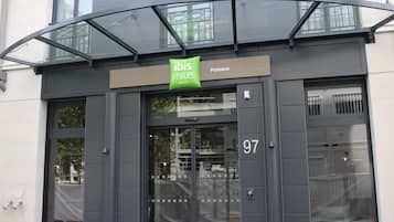 A hotel entrance with a glass canopy, a sign for 'ibis Styles Hotels,' and the number '97' on the door.