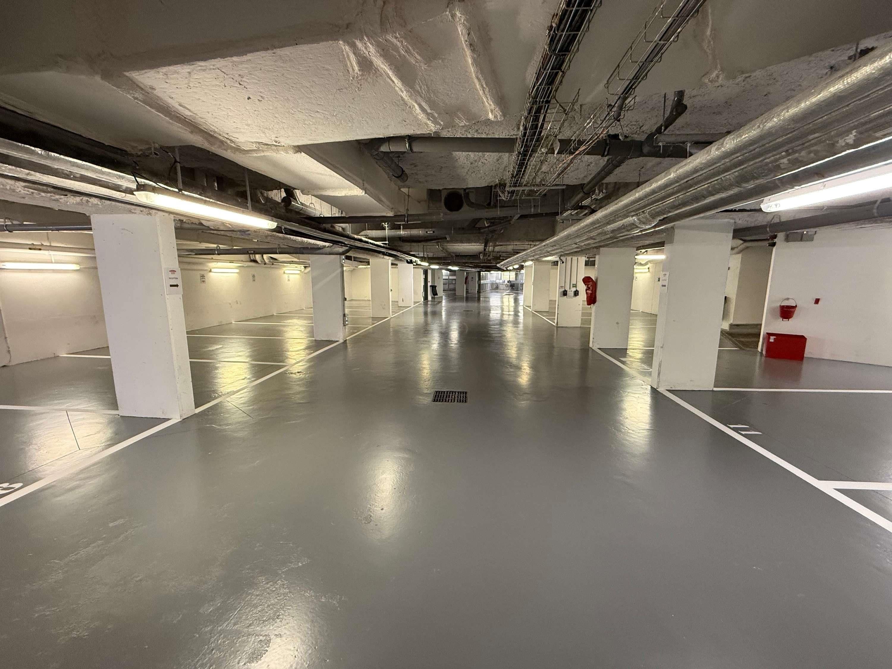 An underground parking garage with white pillars, fluorescent lighting, and a clean, empty floor.