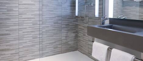Un baño moderno con cabina de ducha de vidrio, lavamanos empotrado y perchero.