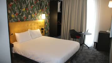 A hotel room with a large bed, a desk with a laptop, a chair, a wardrobe, and a curtain.