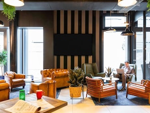 A modern lobby with leather sofas, a flat-screen TV, and a man using a laptop.