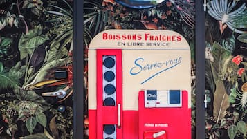A red vending machine with a mirror above it, surrounded by a lush, tropical wallpaper.