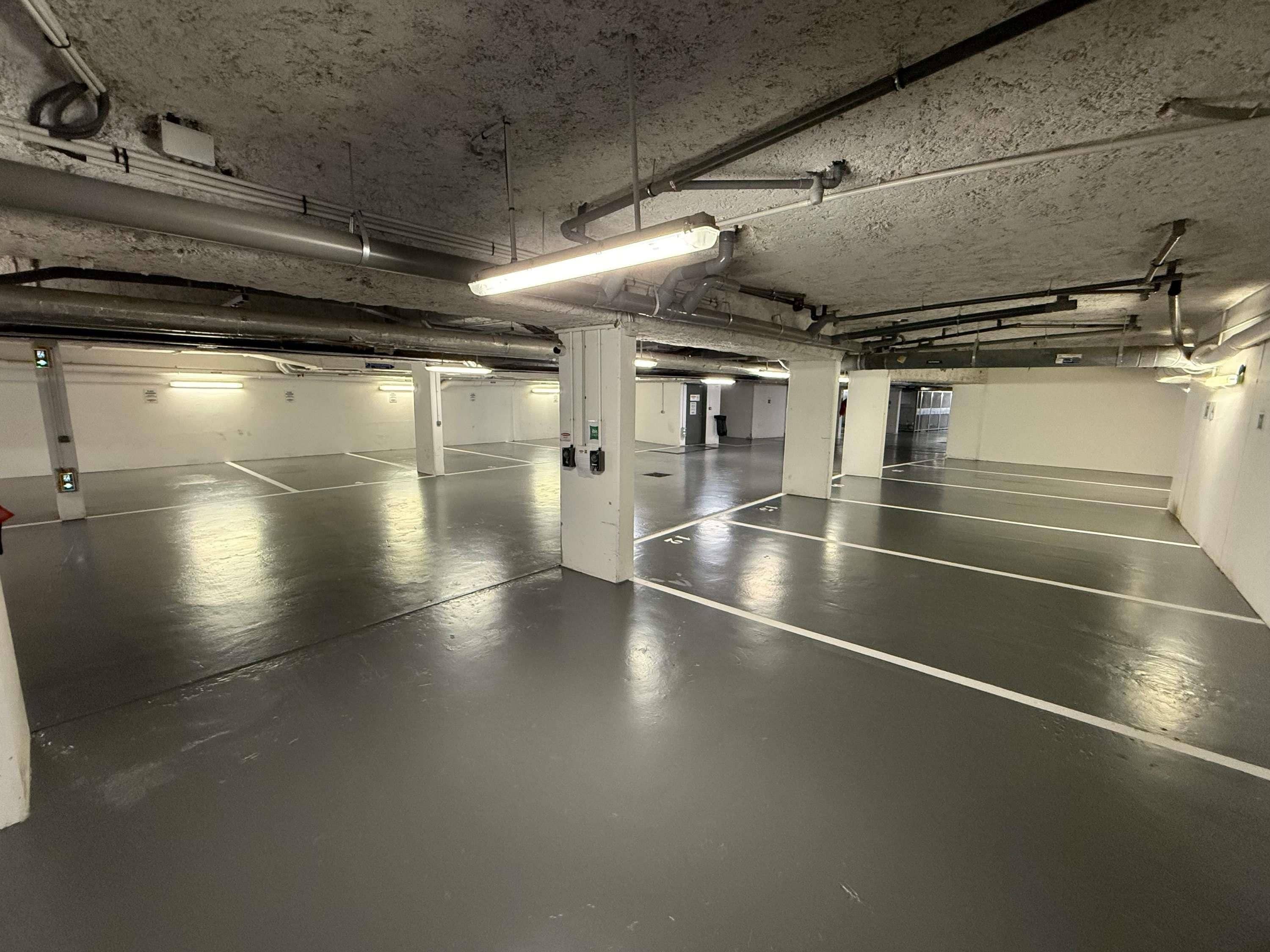 An underground parking garage with multiple parking spaces, concrete pillars, and overhead lighting.