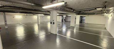 An underground parking garage with multiple parking spaces, concrete pillars, and overhead lighting.