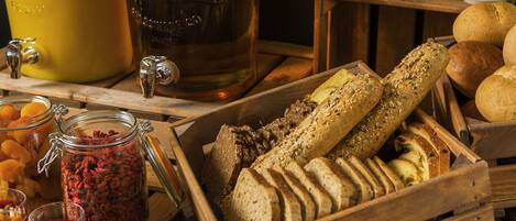 A wooden table with a variety of food items, including jars of preserved fruits and vegetables, a loaf of bread, and a wooden crate filled with sliced bread.