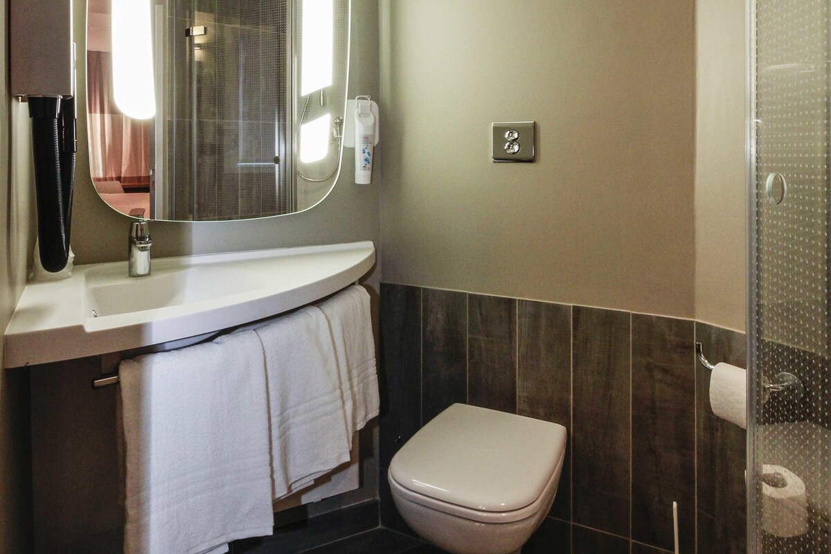A bathroom with a toilet, a sink with a mirror, a towel rack, and a shower area.
