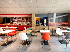 Un restaurante moderno con una decoración en rojo y negro, que presenta una barra con alimentos y una máquina de café. Hay varias mesas y sillas de colores variados.
