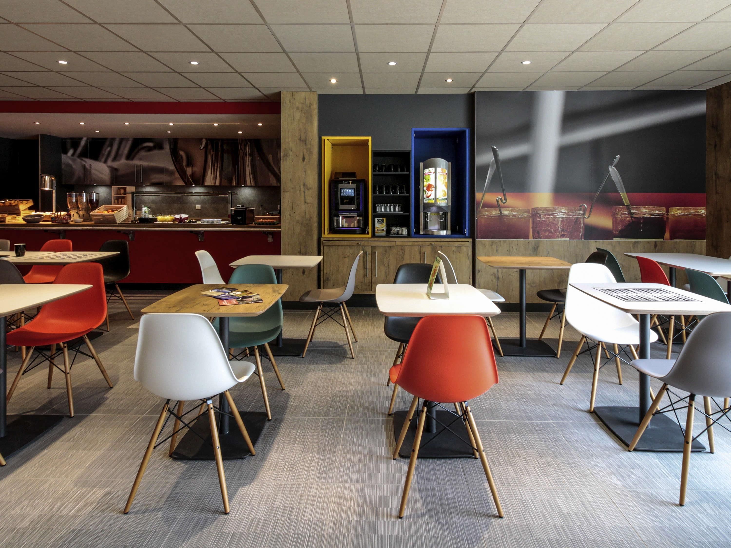 A modern restaurant interior with tables and chairs, a kitchen area, and a bar.