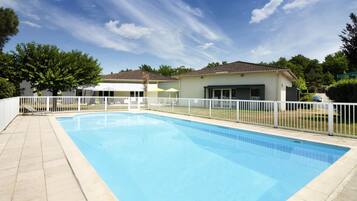 Una piscina rectangular con cerramiento blanco, rodeada por una terraza empavedada.