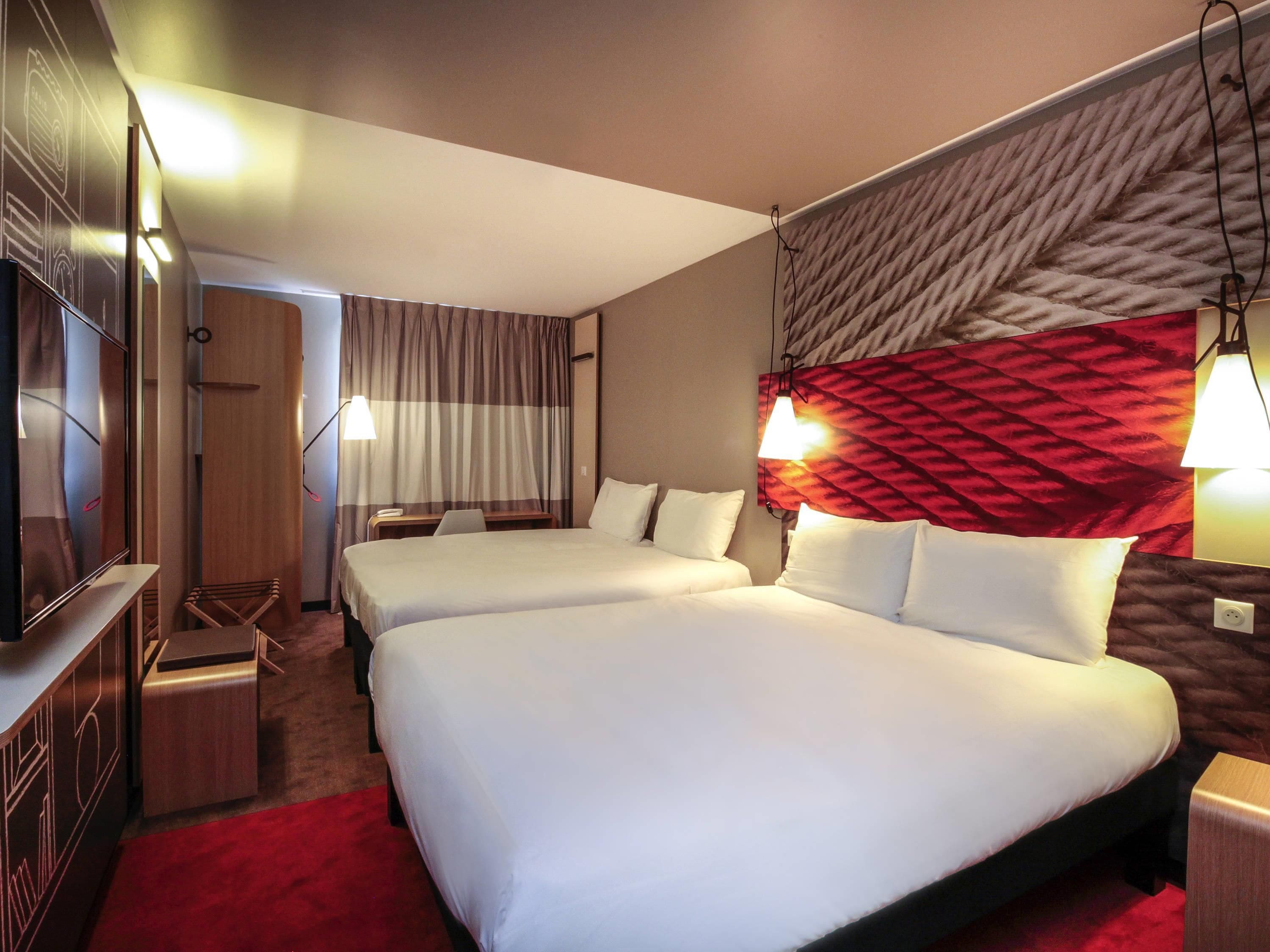 Une chambre d’hôtel avec deux lits, une télévision, un bureau et une moquette rouge.
