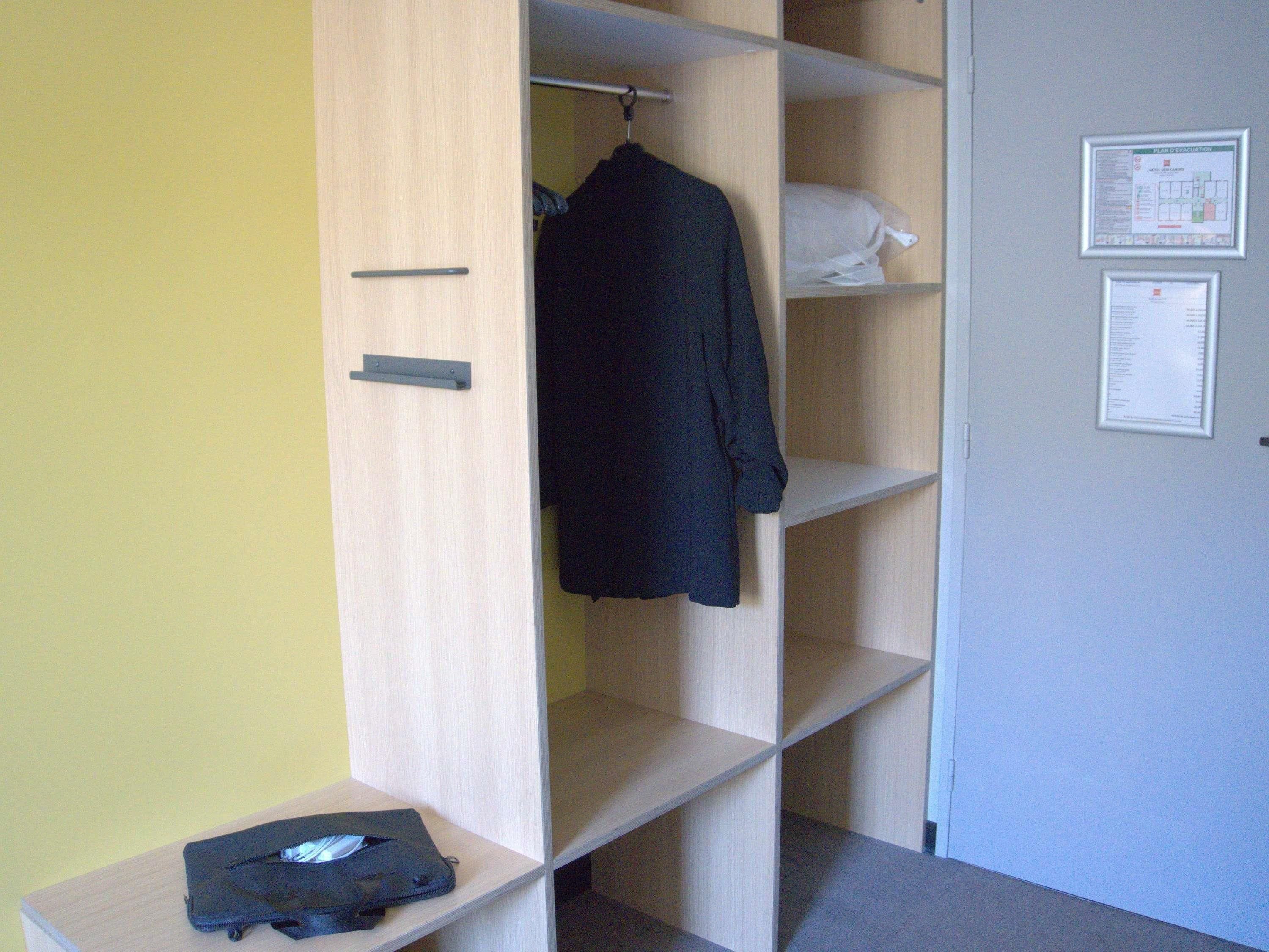 A wardrobe with a hanging rod and shelves, a small table with a bag, and a door with two framed documents.