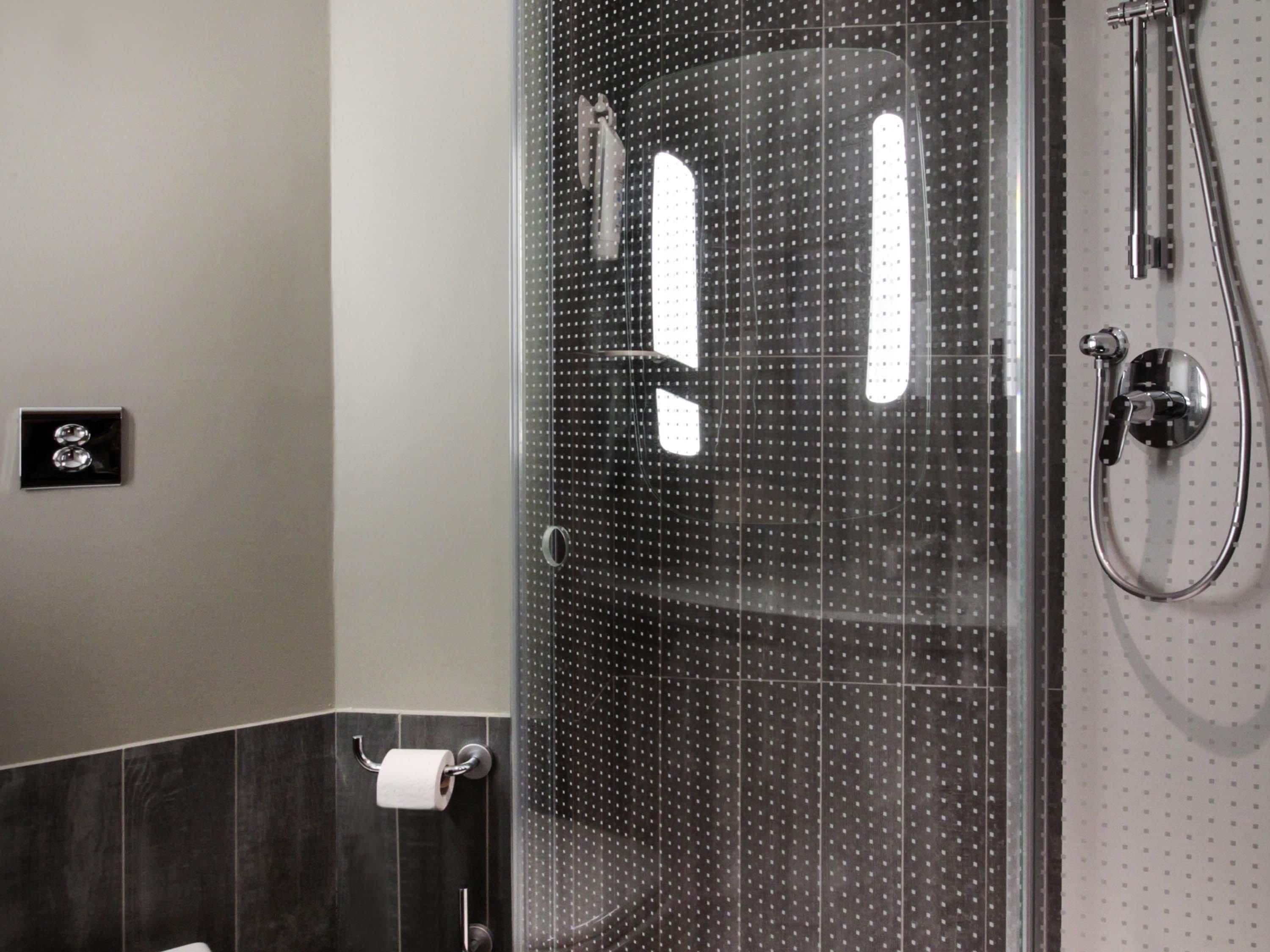 Een douche met een glazen deur, een handdouche en een handdoekhouder.