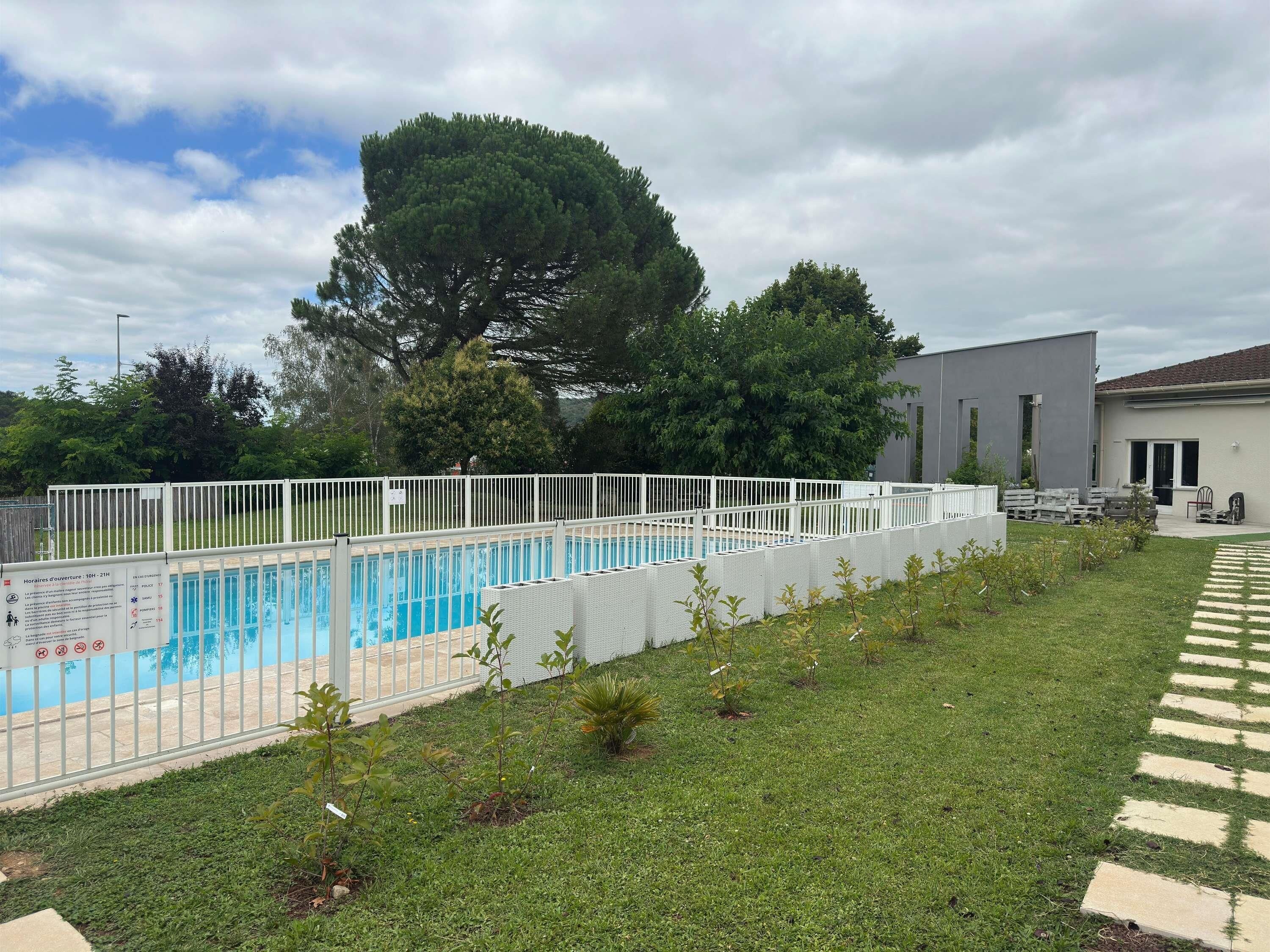 A swimming pool with a white fence, a grassy area, and a building in the background.