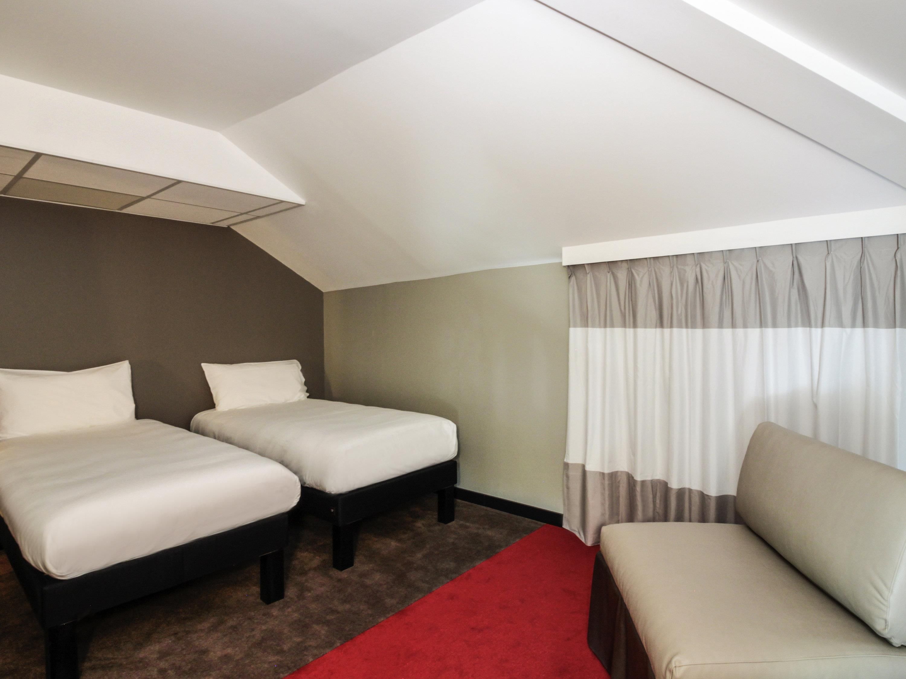 A hotel room with two single beds, a sofa, and a red carpet.