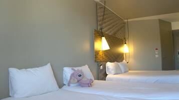Habitación de hotel con dos camas, ropa de cama blanca, un peluche en una cama y una lámpara de pared.