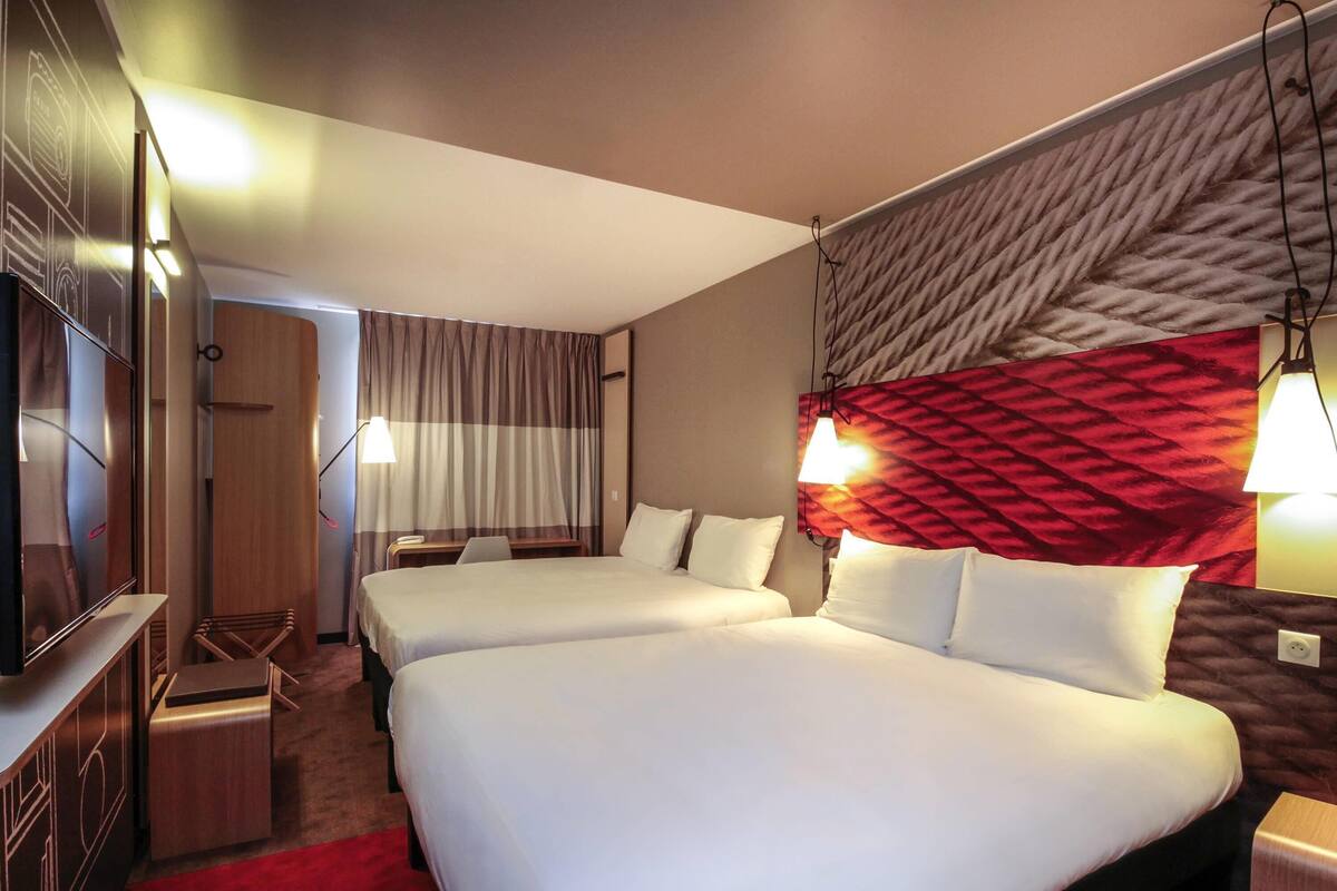 A hotel room with two beds, a TV, a desk, and a red carpet.