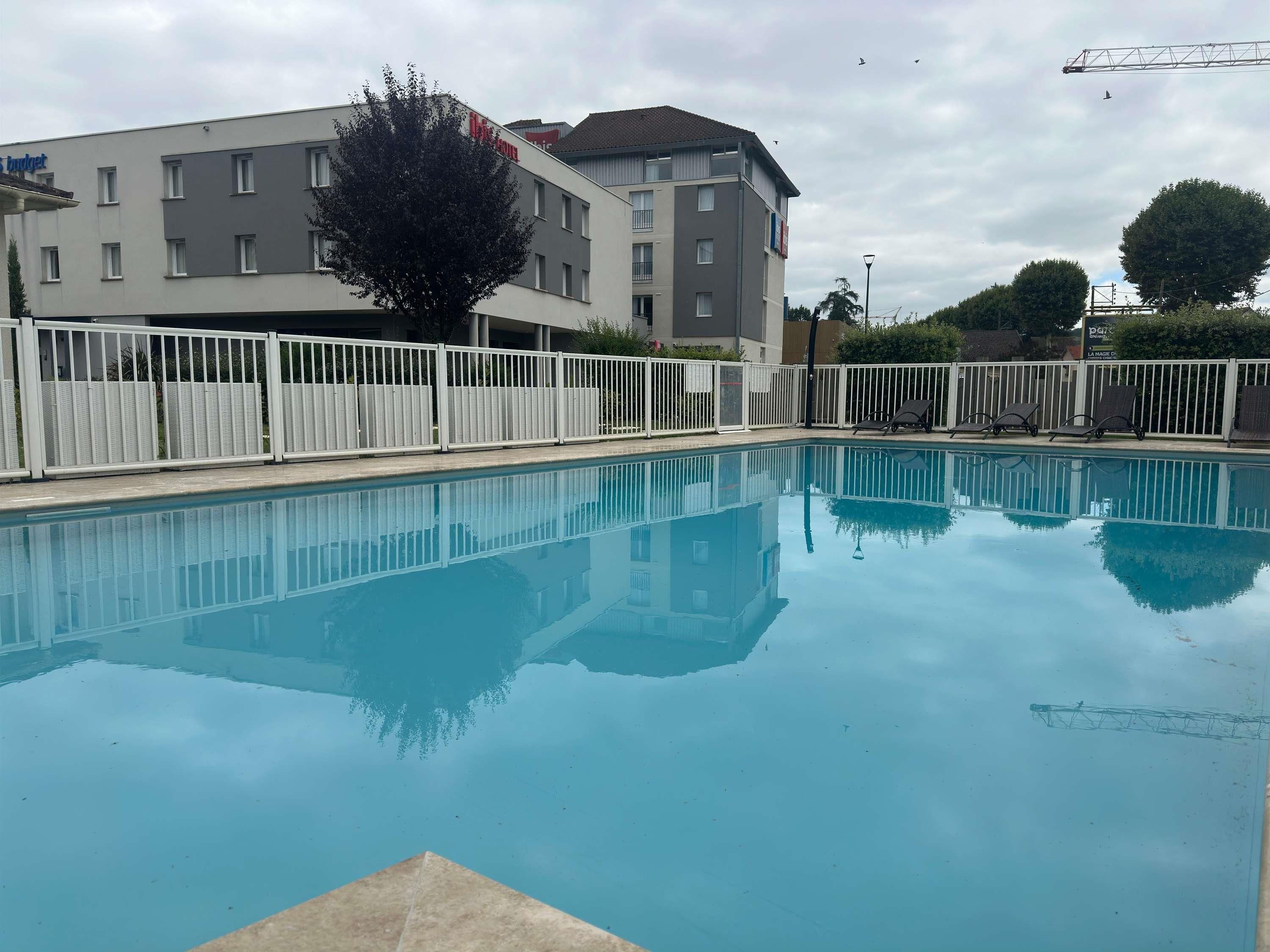 Una piscina con una valla blanca, un edificio con un letrero y un árbol.