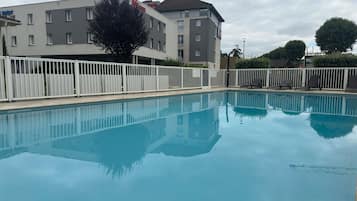Una piscina con una valla blanca, un edificio con un letrero y un árbol.