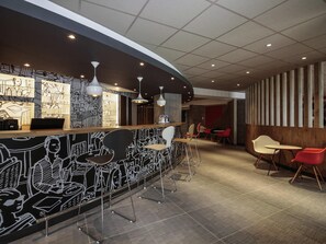 A modern bar area with a curved counter, bar stools, and a wall with black and white illustrations. - ibis Cahors (Cahors)