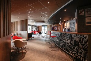 A modern bar area with a mural, wooden paneling, and red chairs. - ibis Cahors (Cahors)