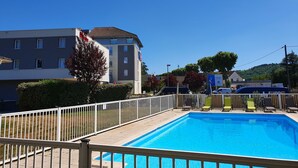A swimming pool with a white fence, a building with multiple windows, and a clear blue sky. - ibis Cahors (Cahors)