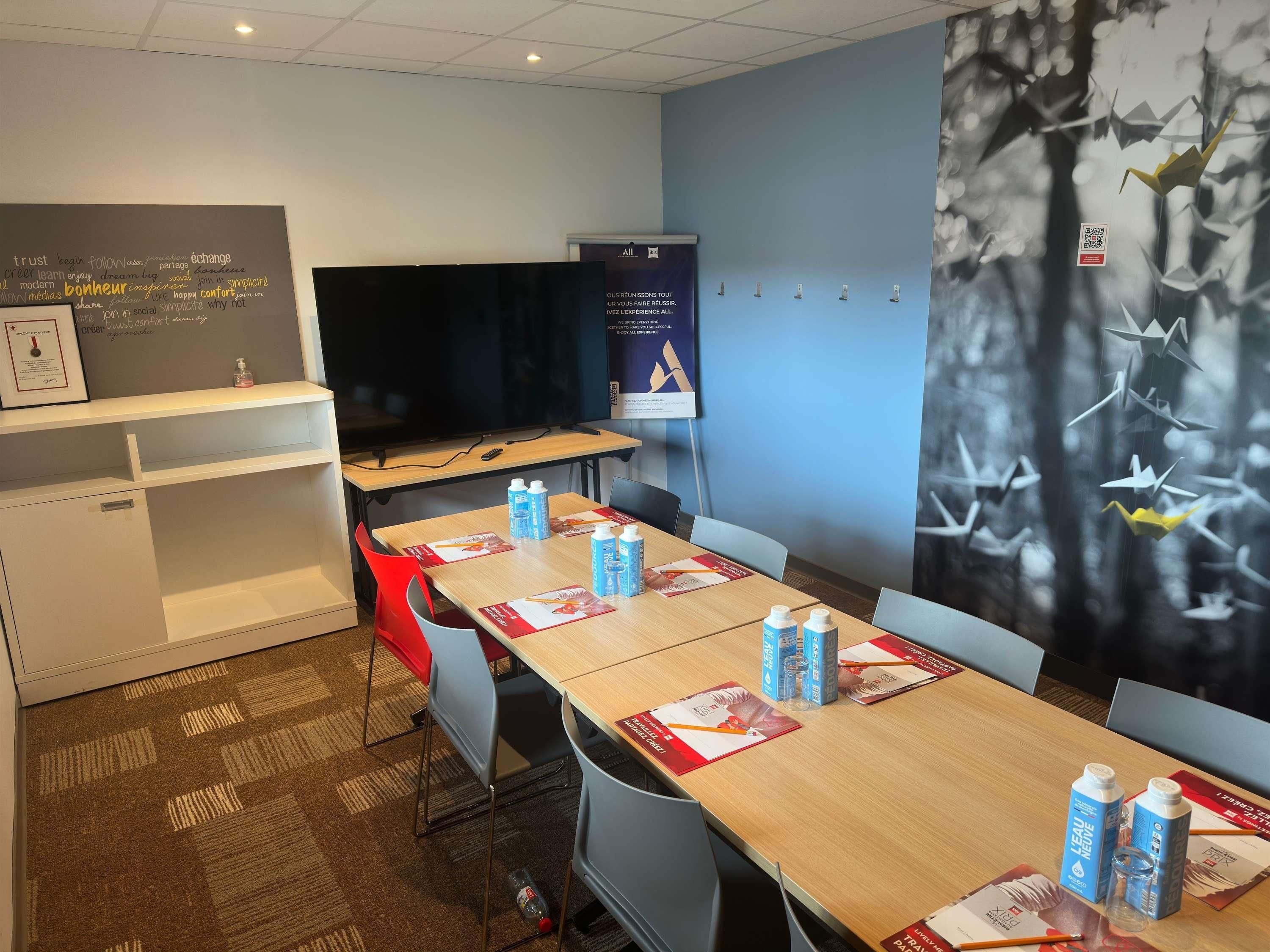 Un salón de conferencias con mesas, sillas, una pantalla de proyector, una pizarra y una pared con un código QR.