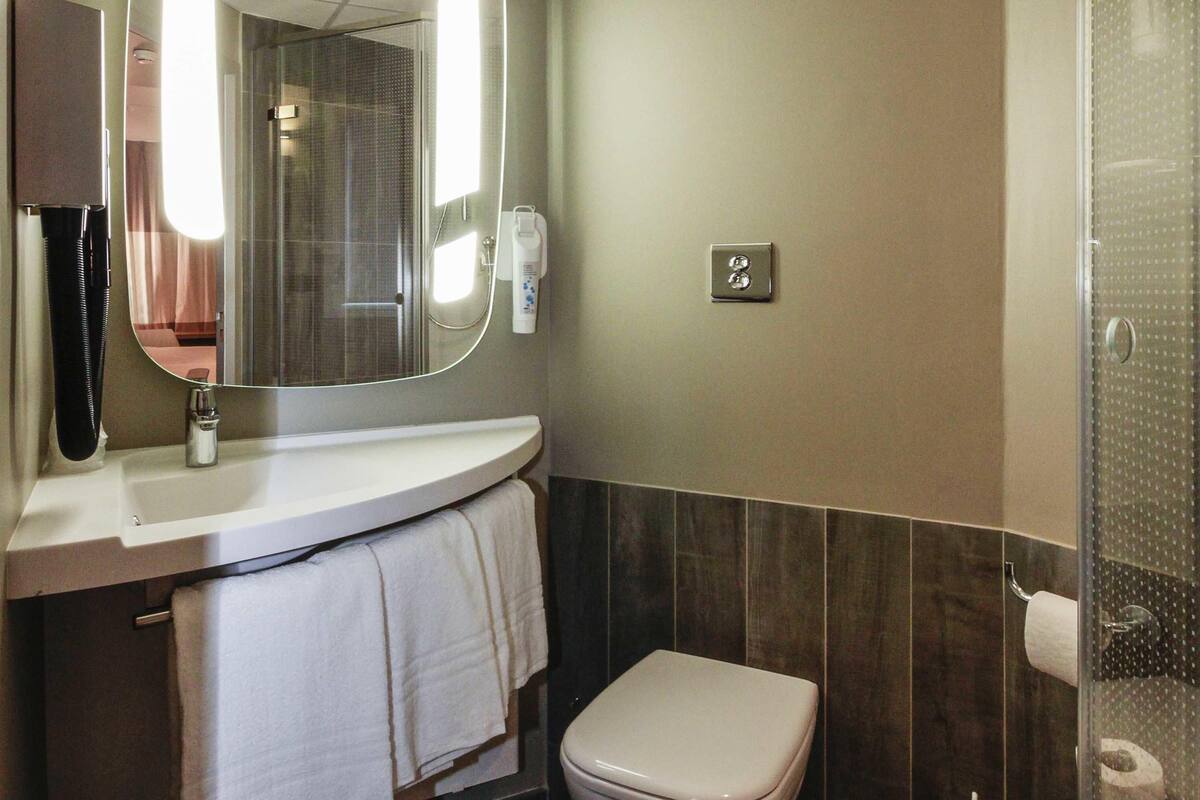 A bathroom with a toilet, a sink with a mirror, a towel rack, and a shower area.