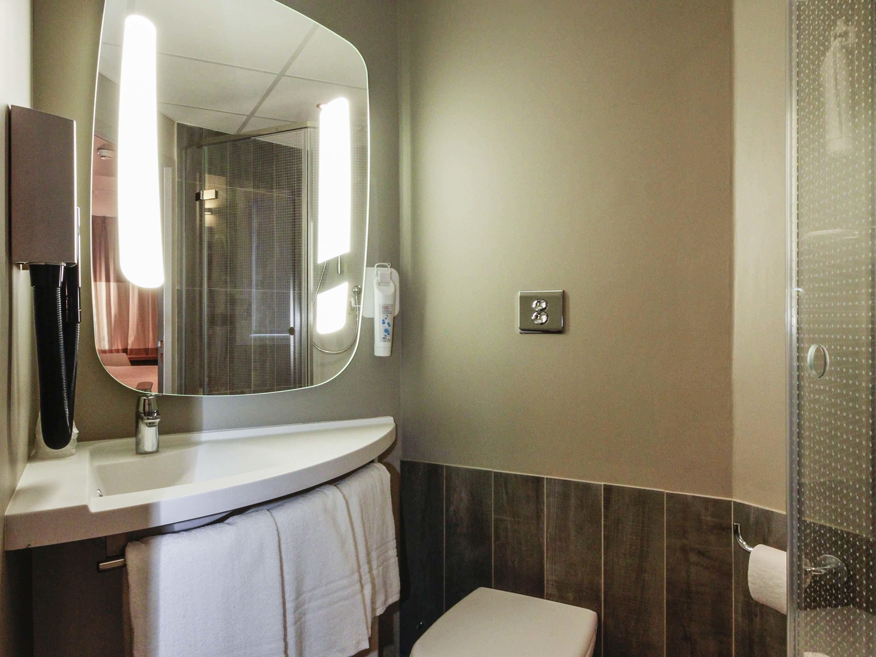 Een badkamer met een ronde spiegel, een witte wastafel, toilet en douche.