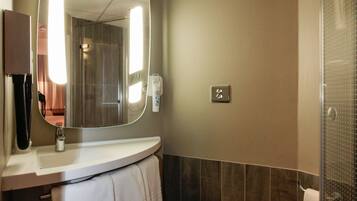Un baño moderno con un espejo curvo, un inodoro, un lavabo y una zona de ducha.