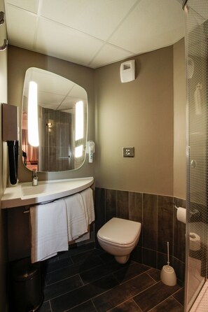Un baño moderno con un espejo curvo, un inodoro, un lavabo y una zona de ducha.
