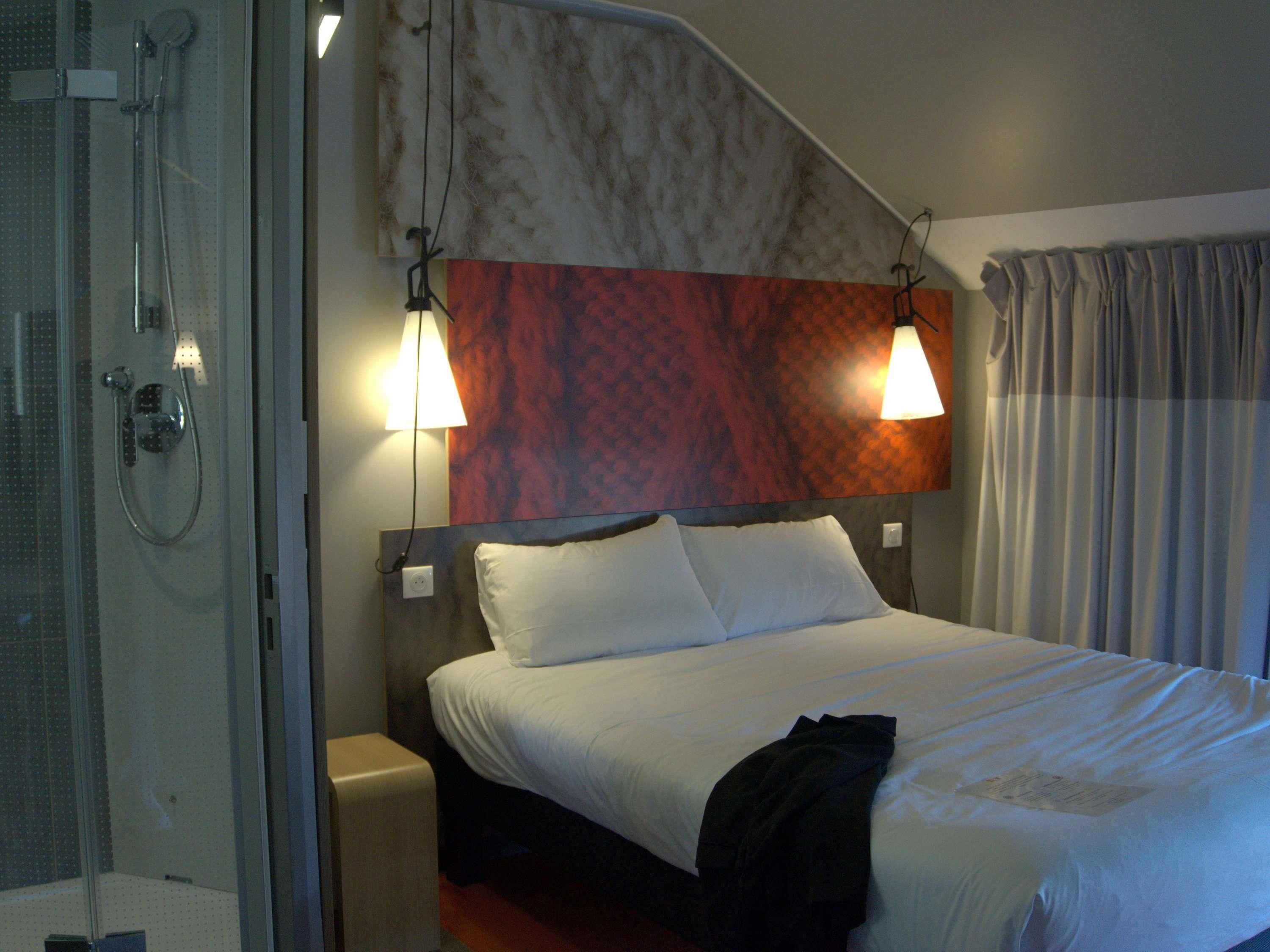 A hotel room with a shower, a bed with white linens, and a headboard with a textured design.