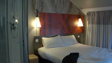 Habitación de hotel con ducha, cama con ropa blanca y cabecera con diseño texturizado.