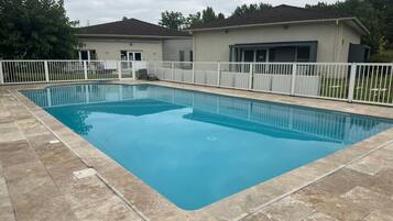 A rectangular swimming pool with a tiled deck, surrounded by a white fence.