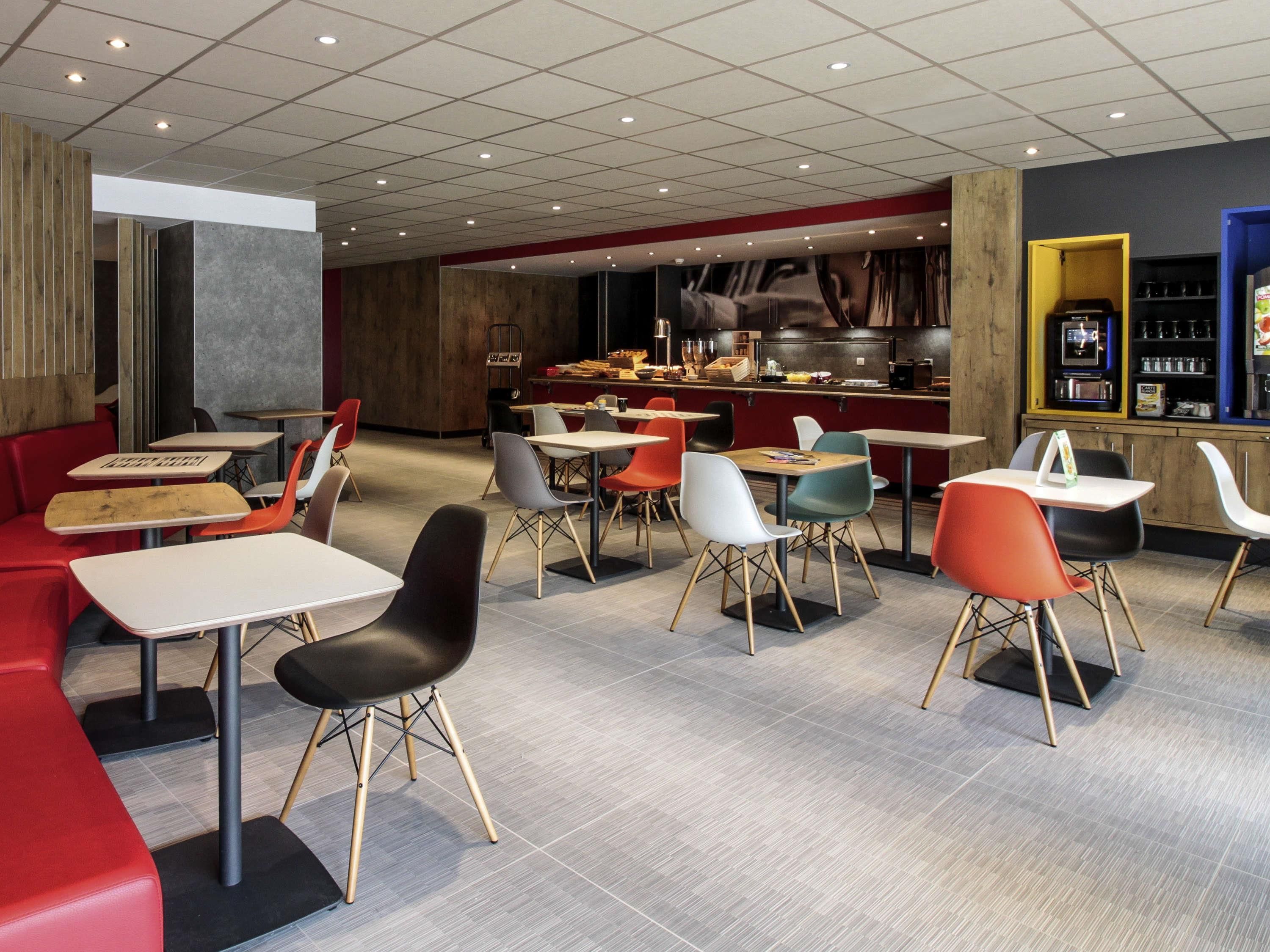 A modern restaurant with a mix of seating options including tables and booths, a visible kitchen area, and a bar.