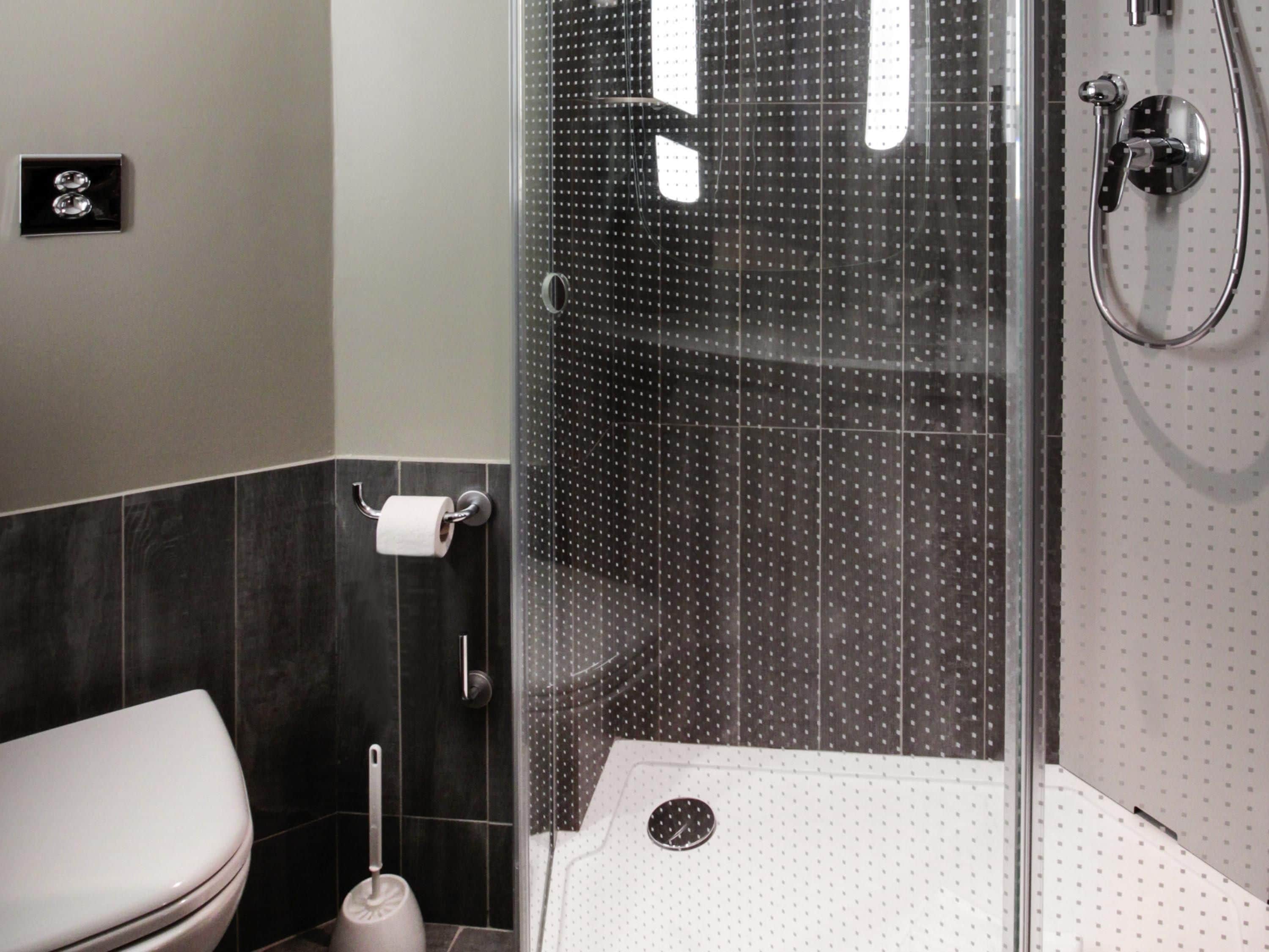 Et moderne badeværelse med toilet, brusekabine med glasdør og toiletpapirholder.