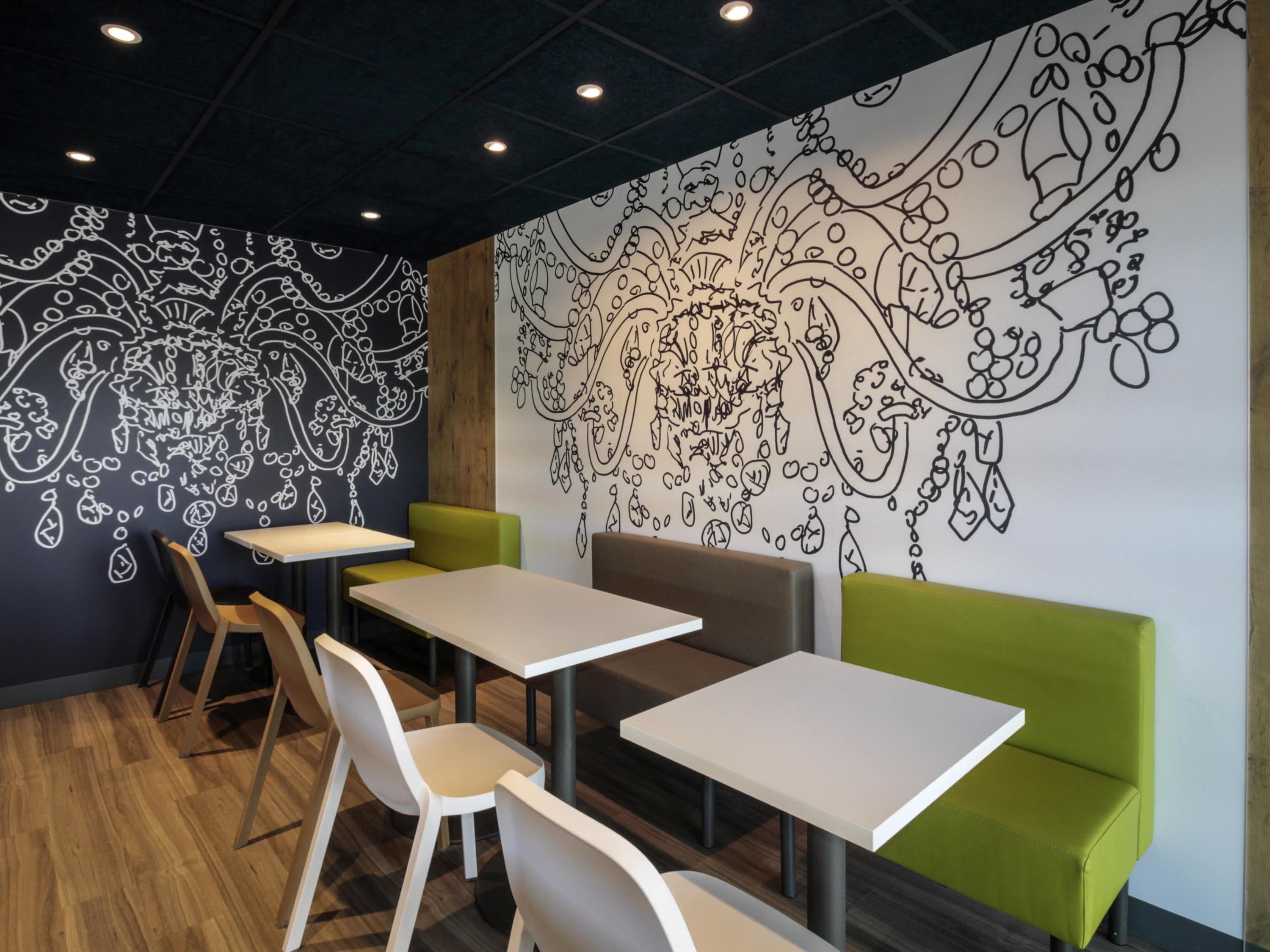 Un interior moderno con mesas y sillas, un mural grande en la pared y un banco acolchado verde.