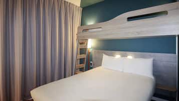 Een hotelkamer met een stapelbed, een houten hoofdbord, een groot raam met gordijnen en een nachtkastje met een lamp.