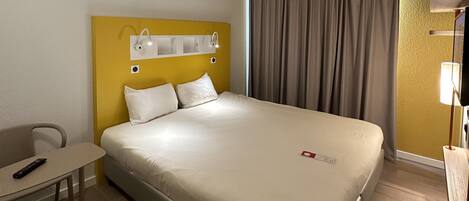 Una habitación de hotel con una cama, un escritorio, una silla y una mesita de noche.
