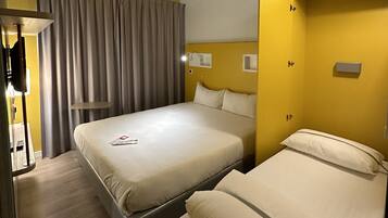Ein Hotelzimmer mit zwei Betten, einem Schreibtisch, einer Lampe und einem Vorhang.
