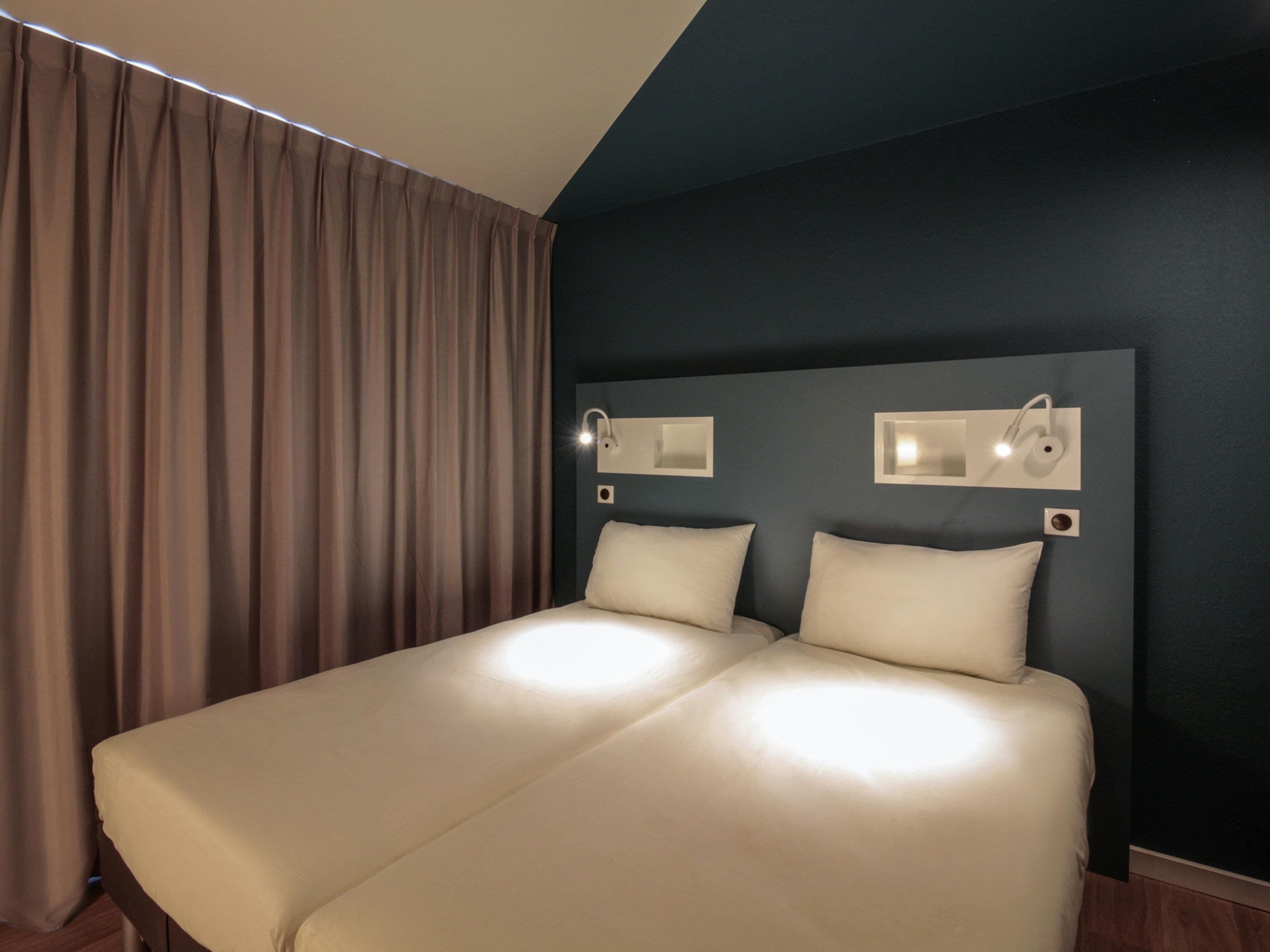A double bed with a headboard, two bedside tables, and a large window with curtains.