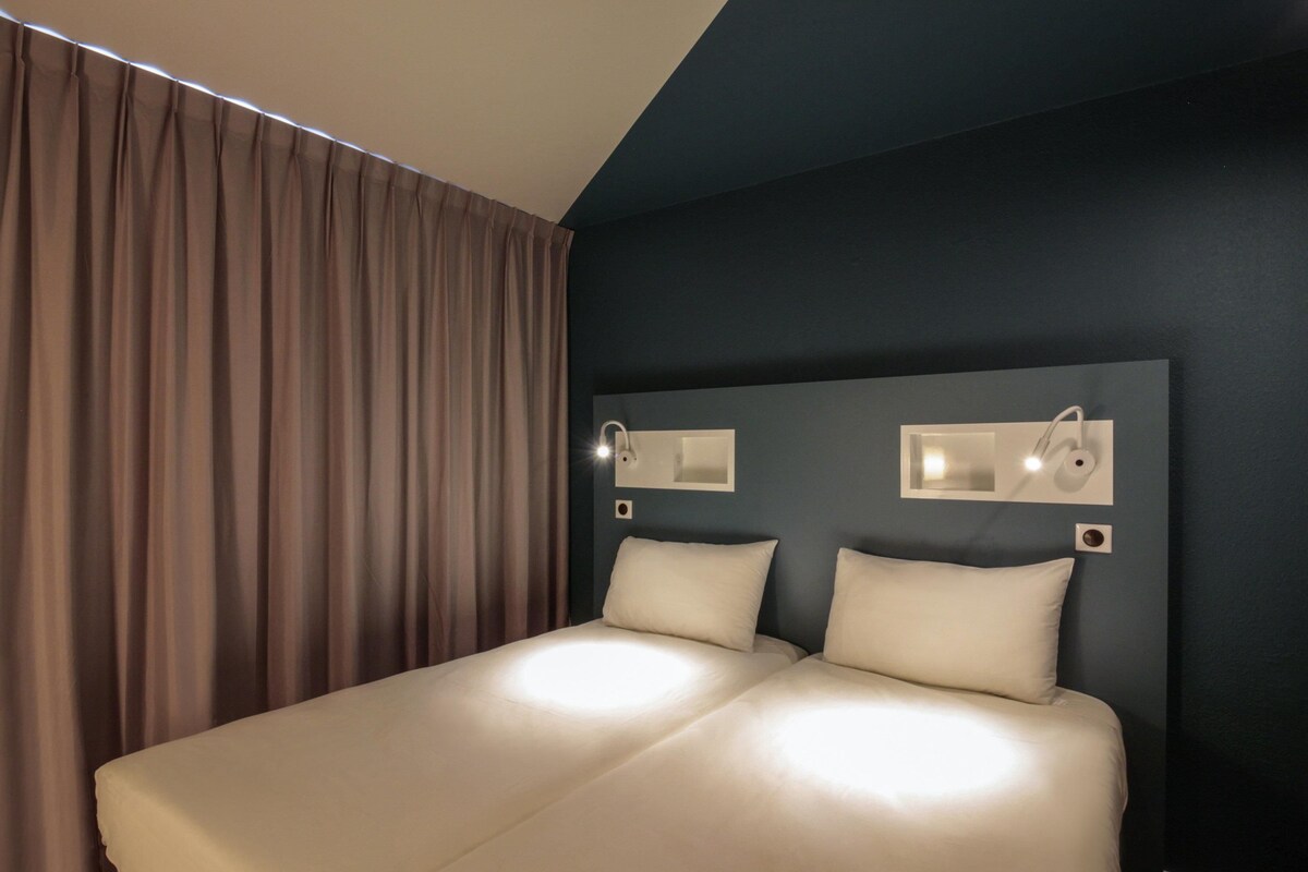 A double bed with a headboard, two bedside tables, and a large window with curtains.