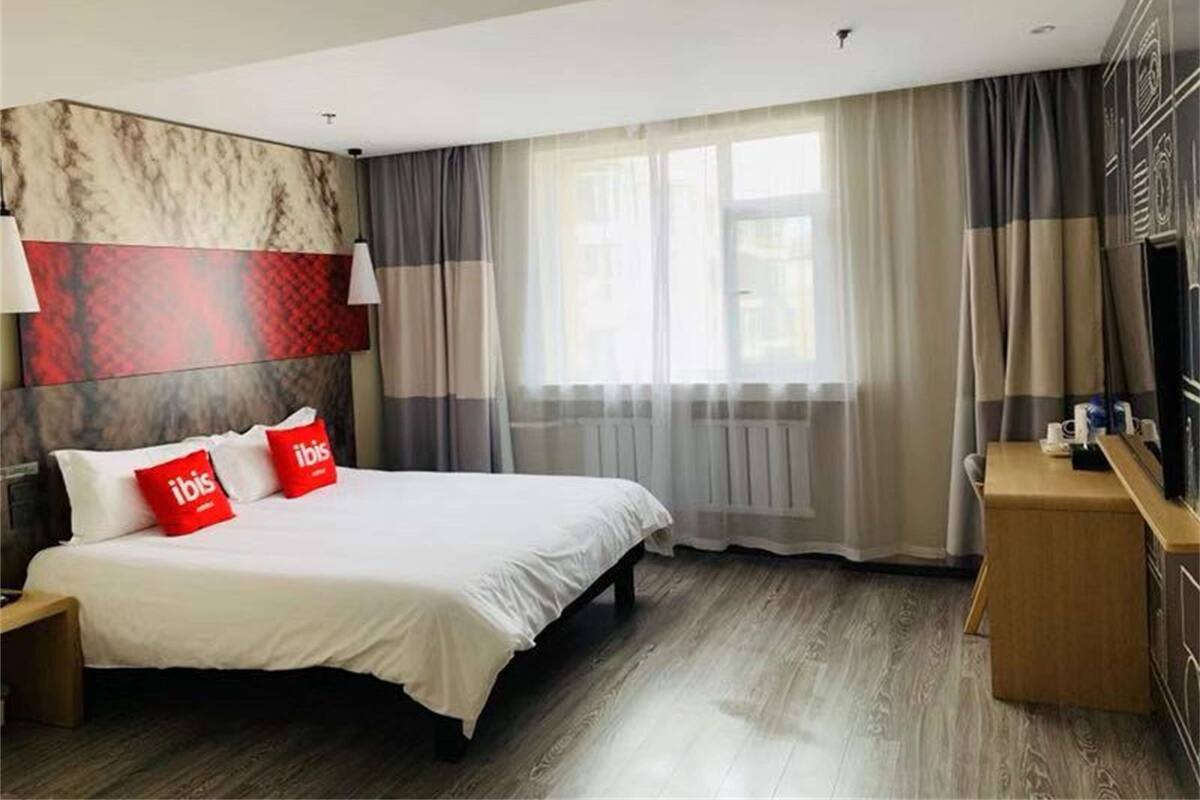 A hotel room with a bed, a desk, a TV, and a window with curtains.