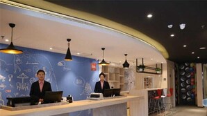 A modern reception desk with two staff members, a blue wall with white doodles, and a curved ceiling with pendant lights. - Ibis Jilin Beishan Park Hotel (Jilin)