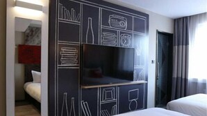 A hotel room with a large flat-screen TV mounted on a black wall with white geometric designs. There are two beds with white linens, a wooden floor, and a window with curtains. - Ibis Jilin Beishan Park Hotel (Jilin)