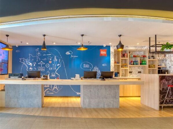 Un moderno hall de hotel con mostrador de recepción, una pared azul con ilustraciones de viajes y una estantería con diversos objetos.