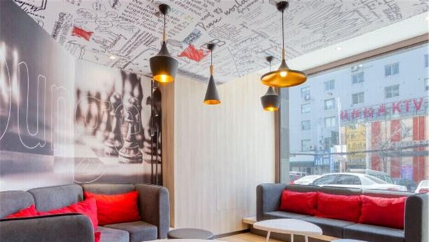 A modern lounge area with grey sofas, red cushions, and a large window offering a view of the city. - Ibis Jilin Beishan Park Hotel (Jilin)