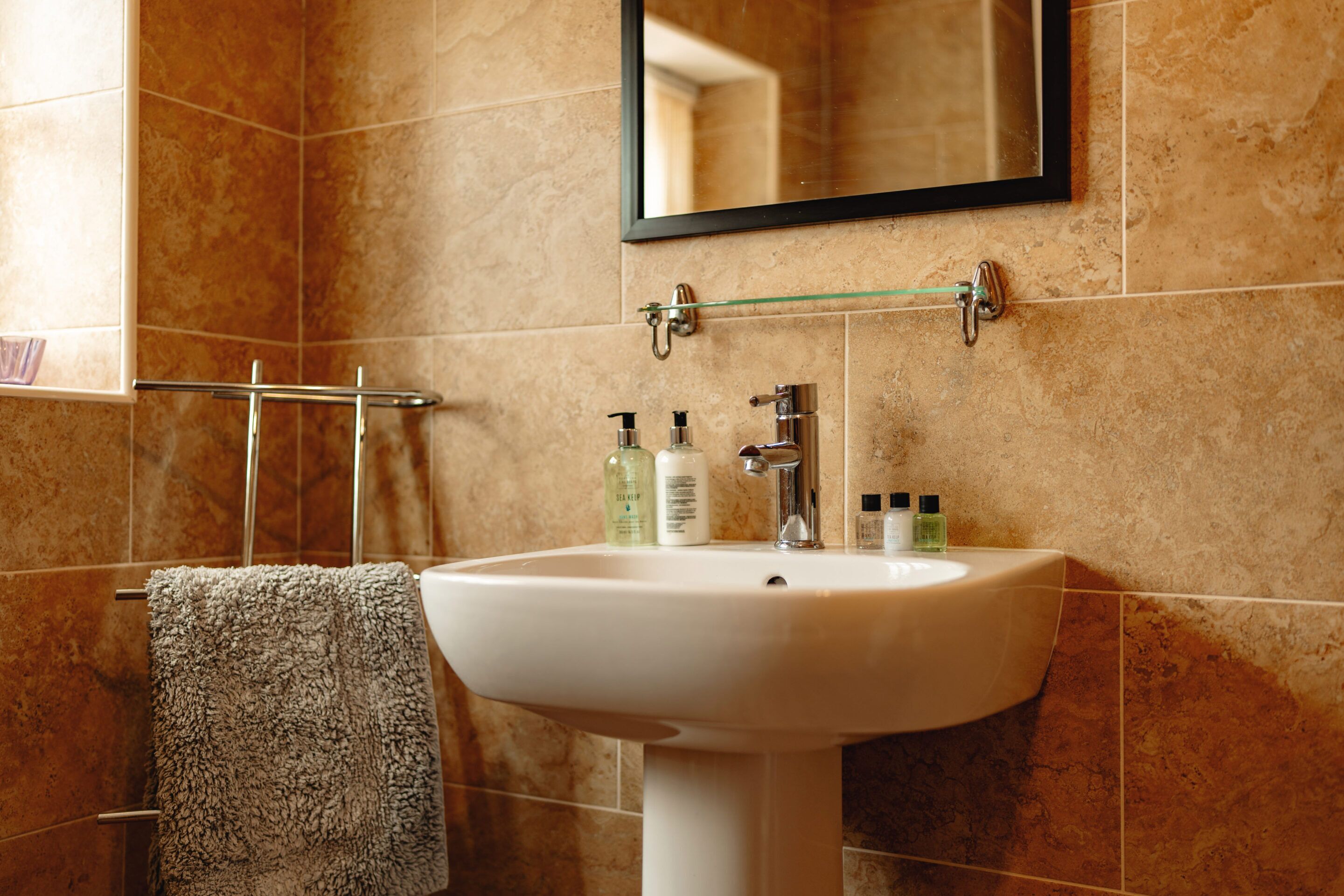 A bathroom with a white sink, a mirror, and toiletries on the wall.